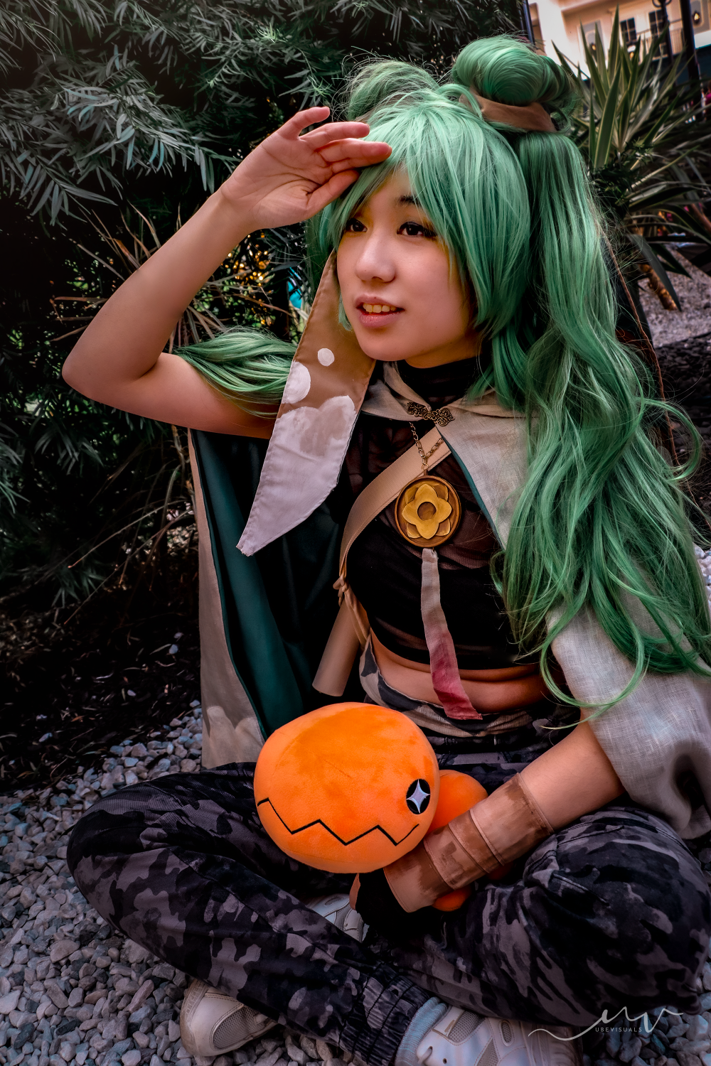 Miku cosplayer sitting on the ground in front of a tropical background, holding a Trapinch.